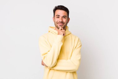 young handsome hicpanic man smiling, enjoying life, feeling happy, friendly, satisfied and carefree with hand on chin