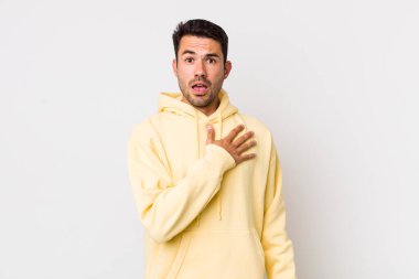 young handsome hicpanic man feeling shocked, astonished and surprised, with hand on chest and open mouth, saying who, me?