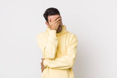 young handsome hicpanic man looking stressed, ashamed or upset, with a headache, covering face with hand
