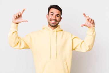 young handsome hicpanic man framing or outlining own smile with both hands, looking positive and happy, wellness concept