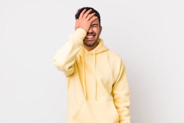 young handsome hicpanic man laughing and slapping forehead like saying doh! I forgot or that was a stupid mistake 