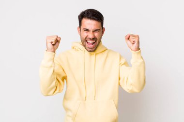 young handsome hicpanic man feeling happy, surprised and proud, shouting and celebrating success with a big smile