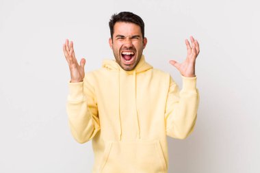young handsome hicpanic man furiously screaming, feeling stressed and annoyed with hands up in the air saying why me