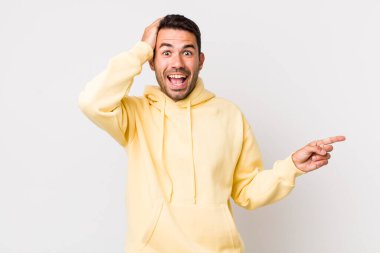 young handsome hicpanic man laughing, looking happy, positive and surprised, realizing a great idea pointing to lateral copy space