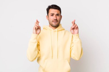 young handsome hicpanic man crossing fingers anxiously and hoping for good luck with a worried look