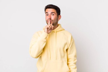 young handsome hicpanic man asking for silence and quiet, gesturing with finger in front of mouth, saying shh or keeping a secret