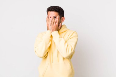 young handsome hicpanic man feeling scared or embarrassed, peeking or spying with eyes half-covered with hands