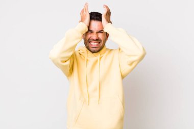young handsome hicpanic man feeling stressed and anxious, depressed and frustrated with a headache, raising both hands to head