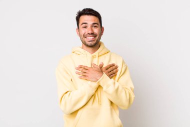 young handsome hicpanic man feeling romantic, happy and in love, smiling cheerfully and holding hands close to heart