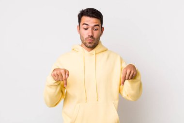 young handsome hicpanic man with open mouth pointing downwards with both hands, looking shocked, amazed and surprised