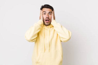 young handsome hicpanic man looking unpleasantly shocked, scared or worried, mouth wide open and covering both ears with hands
