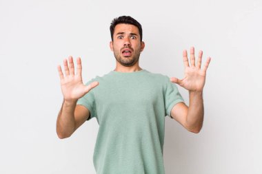 young handsome hicpanic man feeling stupefied and scared, fearing something frightening, with hands open up front saying stay away