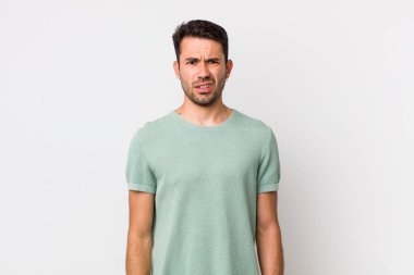 young handsome hicpanic man feeling puzzled and confused, with a dumb, stunned expression looking at something unexpected