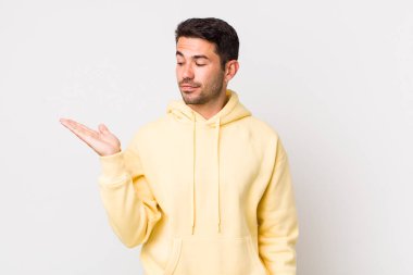 young handsome hicpanic man feeling happy and smiling casually, looking to an object or concept held on the hand on the side