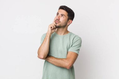 young handsome hicpanic man with a concentrated look, wondering with a doubtful expression, looking up and to the side
