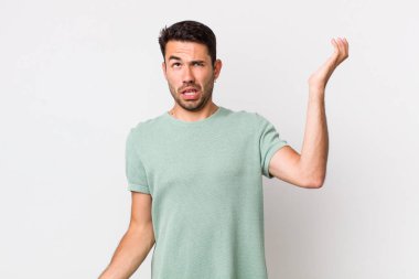 young handsome hicpanic man shrugging with a dumb, crazy, confused, puzzled expression, feeling annoyed and clueless