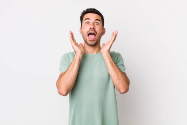 young handsome hicpanic man feeling shocked and excited, laughing, amazed and happy because of an unexpected surprise