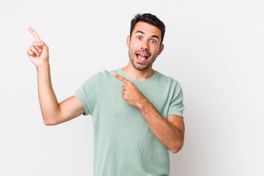 young handsome hicpanic man feeling joyful and surprised, smiling with a shocked expression and pointing to the side