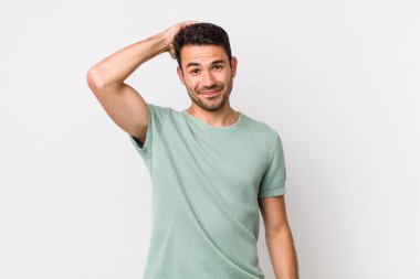 young handsome hicpanic man smiling cheerfully and casually, taking hand to head with a positive, happy and confident look