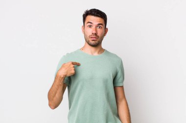 young handsome hicpanic man feeling confused, puzzled and insecure, pointing to self wondering and asking who, me?