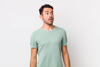 young handsome hicpanic man feeling shocked, happy, amazed and surprised, looking to the side with open mouth