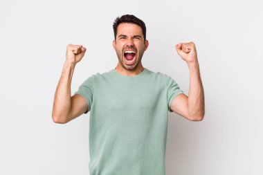 young handsome hicpanic man shouting aggressively with an angry expression or with fists clenched celebrating success