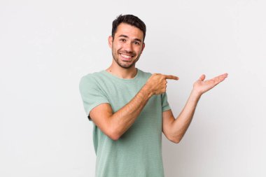 young handsome hicpanic man smiling cheerfully and pointing to copy space on palm on the side, showing or advertising an object