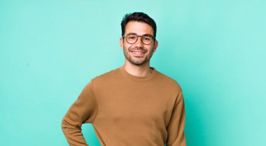 young handsome hicpanic man smiling happily with a hand on hip and confident, positive, proud and friendly attitude