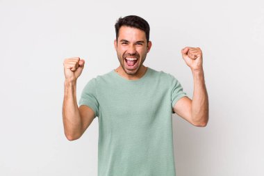 young handsome hicpanic man feeling happy, positive and successful, celebrating victory, achievements or good luck