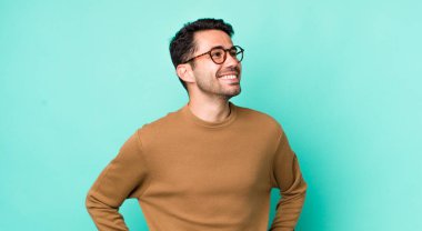 young handsome hicpanic man looking happy, cheerful and confident, smiling proudly and looking to side with both hands on hips