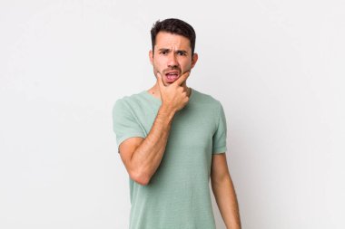 young handsome hicpanic man with mouth and eyes wide open and hand on chin, feeling unpleasantly shocked, saying what or wow