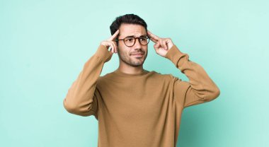 young handsome hicpanic man feeling confused or doubting, concentrating on an idea, thinking hard, looking to copy space on side