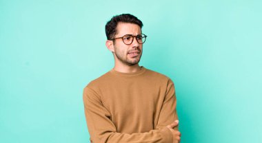 young handsome hicpanic man doubting or thinking, biting lip and feeling insecure and nervous, looking to copy space on the side