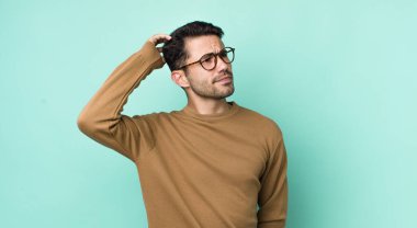 young handsome hicpanic man feeling puzzled and confused, scratching head and looking to the side