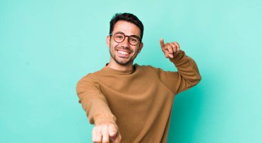 young handsome hicpanic man feeling happy and confident, pointing to camera with both hands and laughing, choosing you