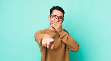 young handsome hicpanic man laughing at you, pointing to camera and making fun of or mocking you