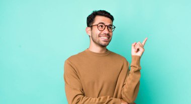 young handsome hicpanic man smiling happily and looking sideways, wondering, thinking or having an idea