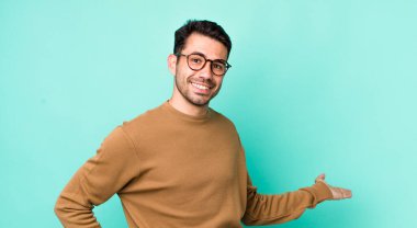 young handsome hicpanic man feeling happy and cheerful, smiling and welcoming you, inviting you in with a friendly gesture