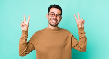 young handsome hicpanic man smiling and looking happy, friendly and satisfied, gesturing victory or peace with both hands