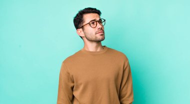 young handsome hicpanic man with a worried, confused, clueless expression, looking up to copy space, doubting