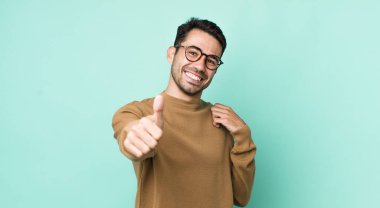 young handsome hicpanic man feeling proud, carefree, confident and happy, smiling positively with thumbs up
