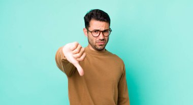 young handsome hicpanic man feeling cross, angry, annoyed, disappointed or displeased, showing thumbs down with a serious look