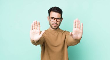 young handsome hicpanic man looking serious, unhappy, angry and displeased forbidding entry or saying stop with both open palms
