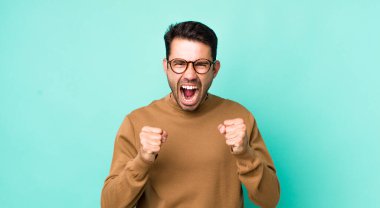 young handsome hicpanic man shouting aggressively with annoyed, frustrated, angry look and tight fists, feeling furious