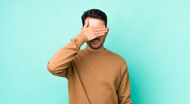 young handsome hicpanic man covering eyes with one hand feeling scared or anxious, wondering or blindly waiting for a surprise