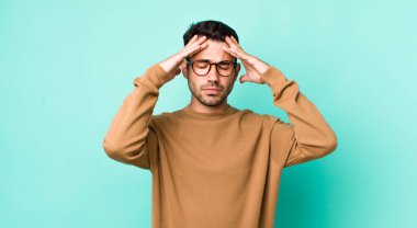 young handsome hicpanic man looking concentrated, thoughtful and inspired, brainstorming and imagining with hands on forehead