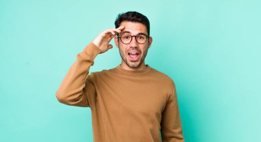 young handsome hicpanic man looking happy, astonished and surprised, smiling and realizing amazing and incredible good news