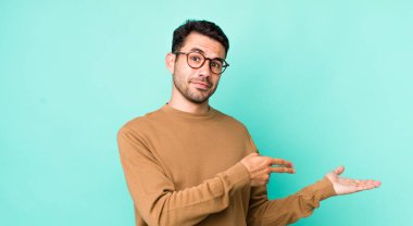 young handsome hicpanic man smiling, feeling happy, carefree and satisfied, pointing to concept or idea on copy space on the side