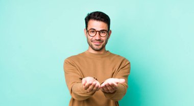 young handsome hicpanic man smiling happily with friendly, confident, positive look, offering and showing an object or concept