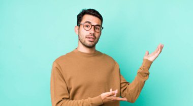 young handsome hicpanic man smiling proudly and confidently, feeling happy and satisfied and showing a concept on copy space